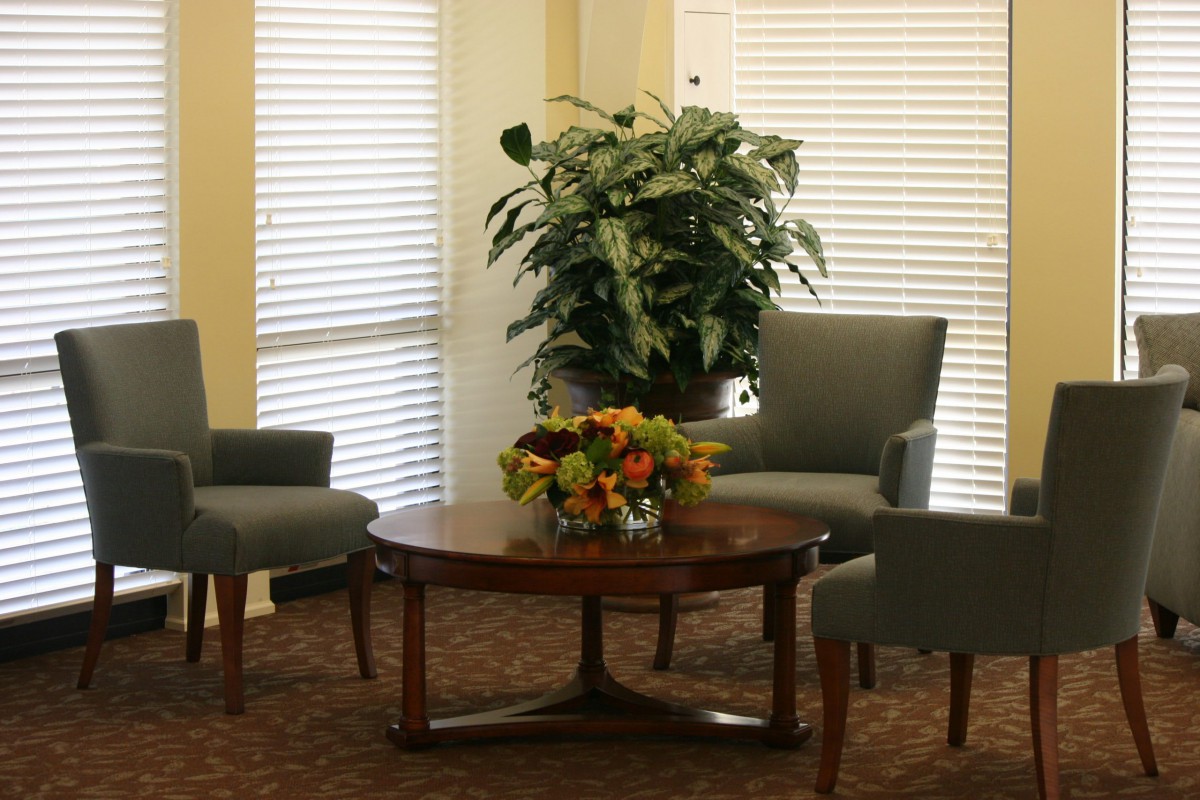 A cozy sitting area with two armchairs, a round wooden table, a large potted plant, and a floral centerpiece.