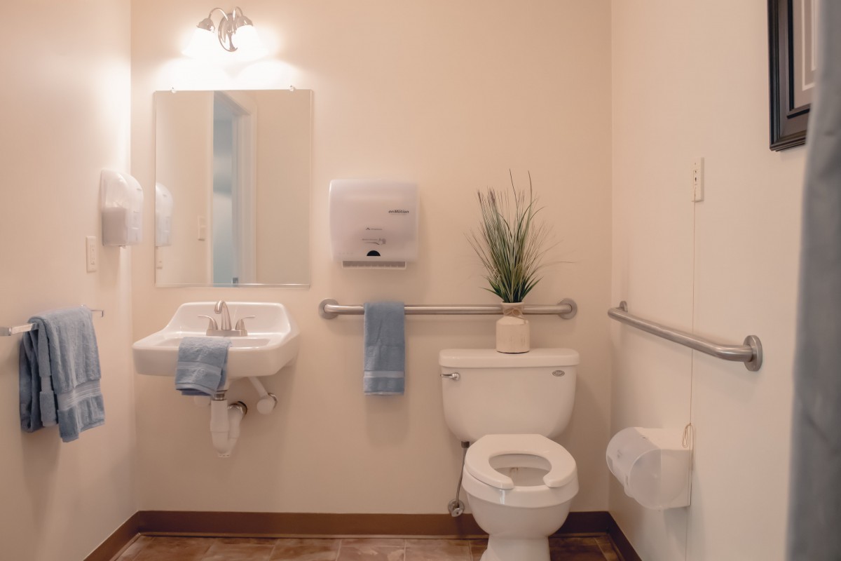 A clean and accessible bathroom with a sink, toilet, and mirror.