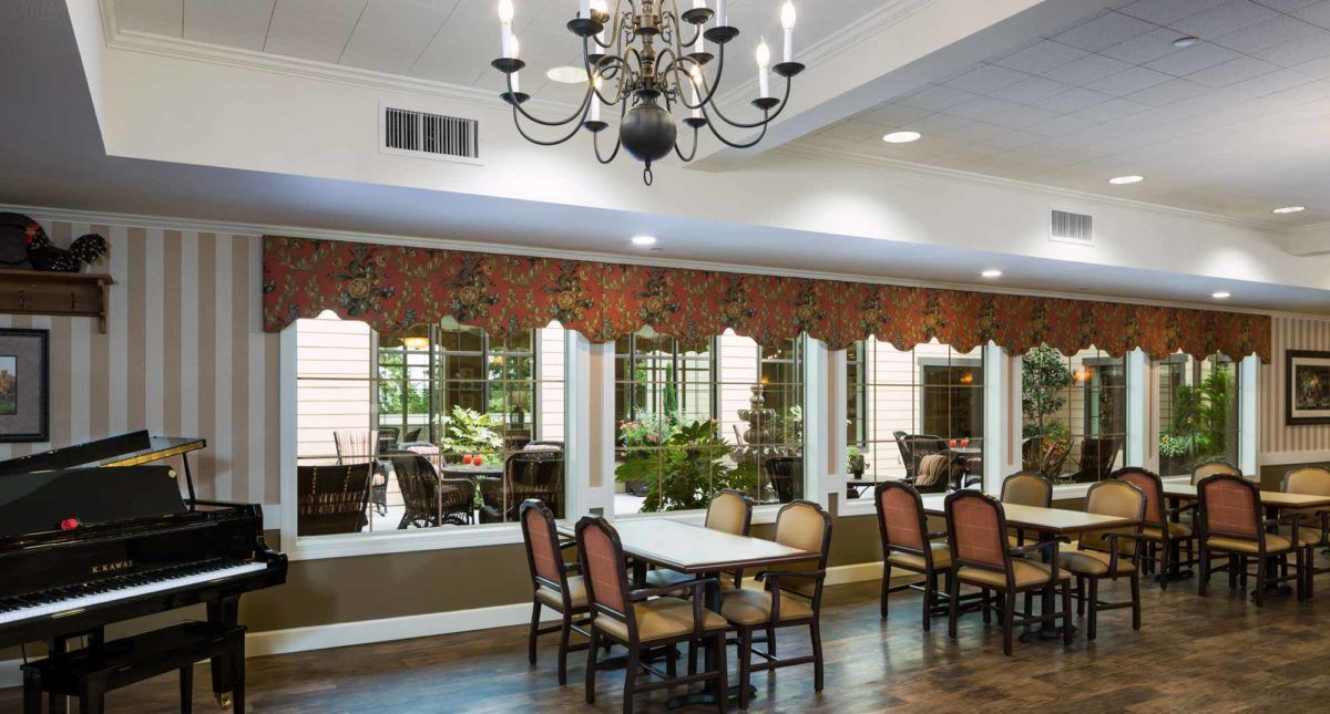 A well-decorated dining room featuring a chandelier, tables, and chairs with large windows and wall decor.