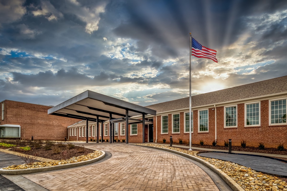A brick building with a covered entrance and a United States flag waving in the breeze under a cloudy sky.