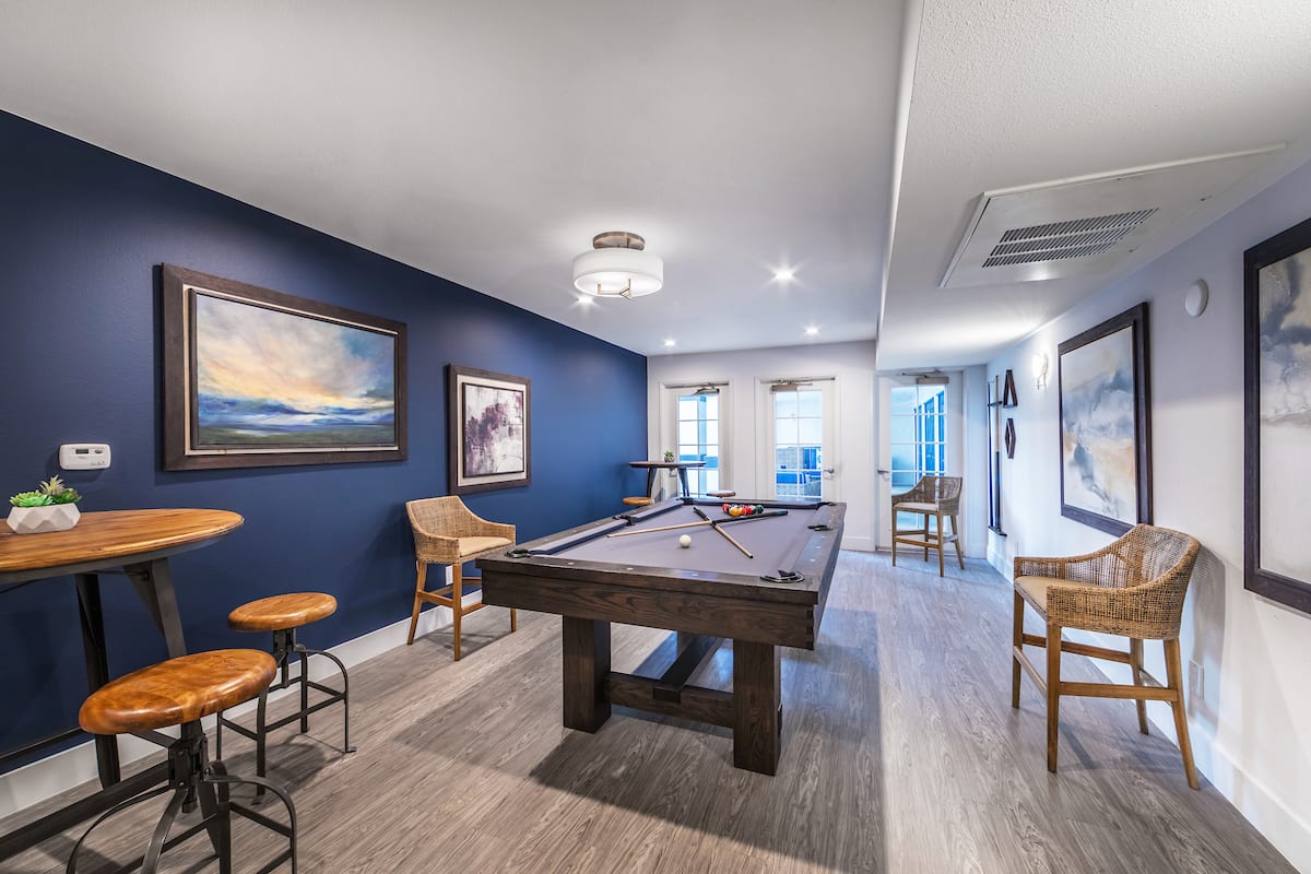 A stylish game room featuring a pool table, artwork on blue walls, and modern furnishings.