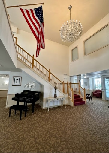 A spacious and elegantly designed lobby featuring a grand staircase, a shining chandelier, an American flag, and tasteful furnishings.