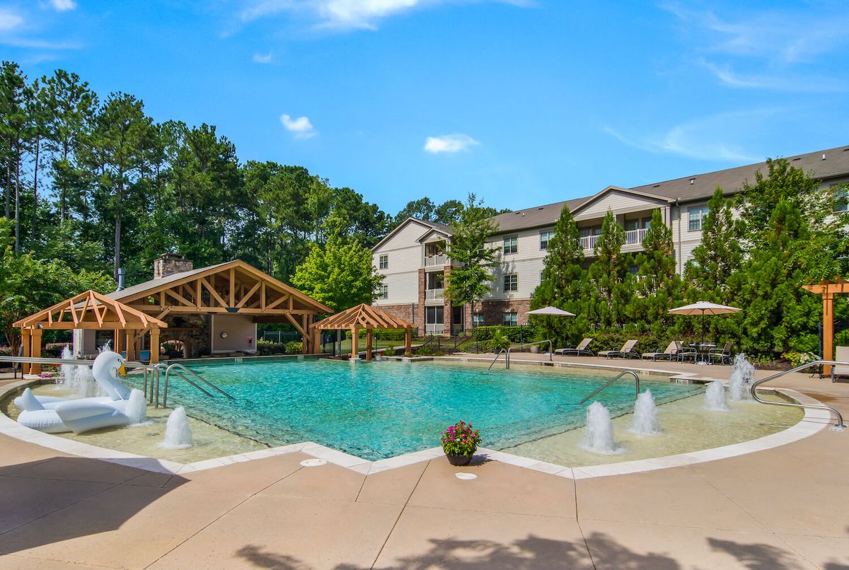 A serene swimming pool area at an apartment complex surrounded by lush greenery and residential buildings.