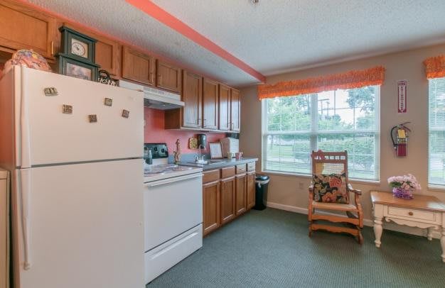A cozy kitchen with wooden cabinets, a white refrigerator and stove, and sunlight streaming through the window.