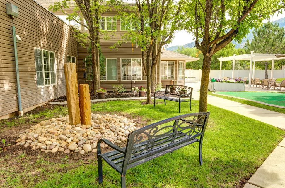 A serene garden area with benches, surrounded by trees and a building in the background.