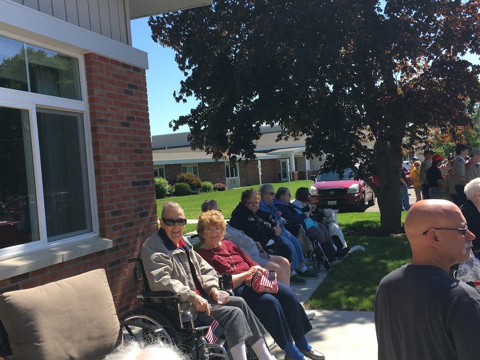 A group of seniors enjoying a sunny day outside, sitting together with some in wheelchairs.