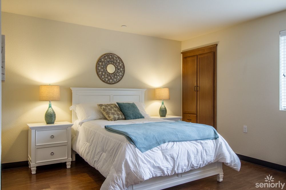 A cozy bedroom with a large bed, decorated with blue and white linens, flanked by two matching lamps on bedside tables, and featuring a wooden wardrobe.