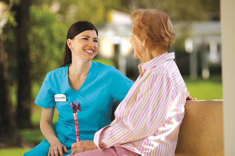 A nurse and an elderly person having a friendly conversation outdoors.