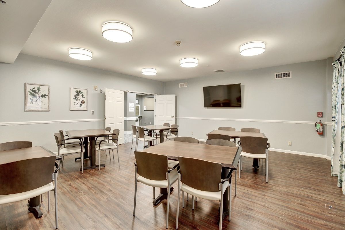 A modern dining area with multiple tables and chairs, featuring a wall-mounted television and wood flooring.