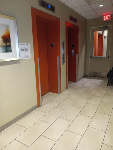 A view of a hallway featuring orange elevator doors, tiled flooring, and a piece of artwork on the wall.