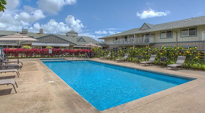A sunny day at a resort with a large swimming pool surrounded by buildings and deck chairs.