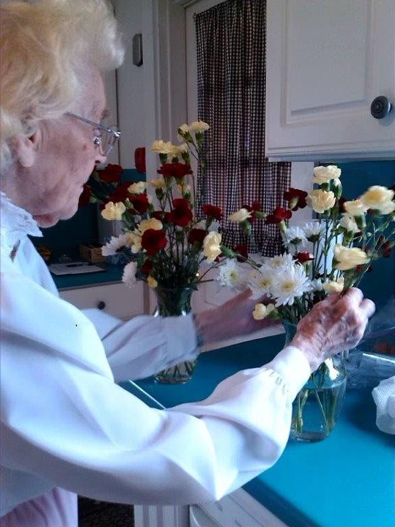 An elderly person arranging flowers in a kitchen.