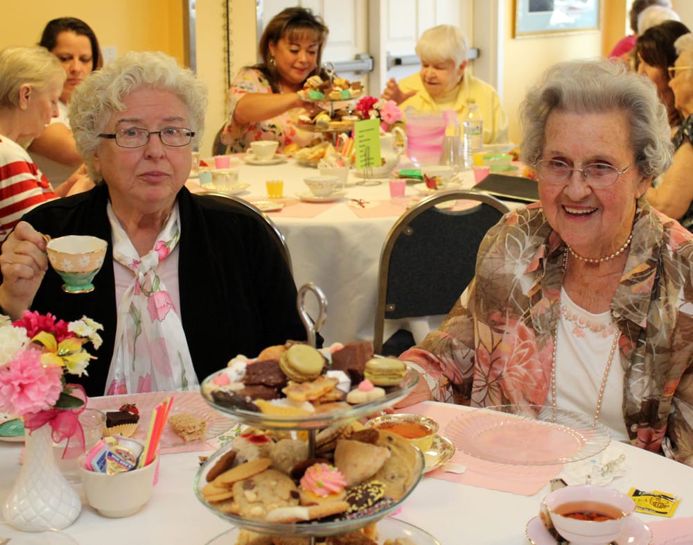 A group of elderly women enjoying an afternoon tea party with cakes and pastries.