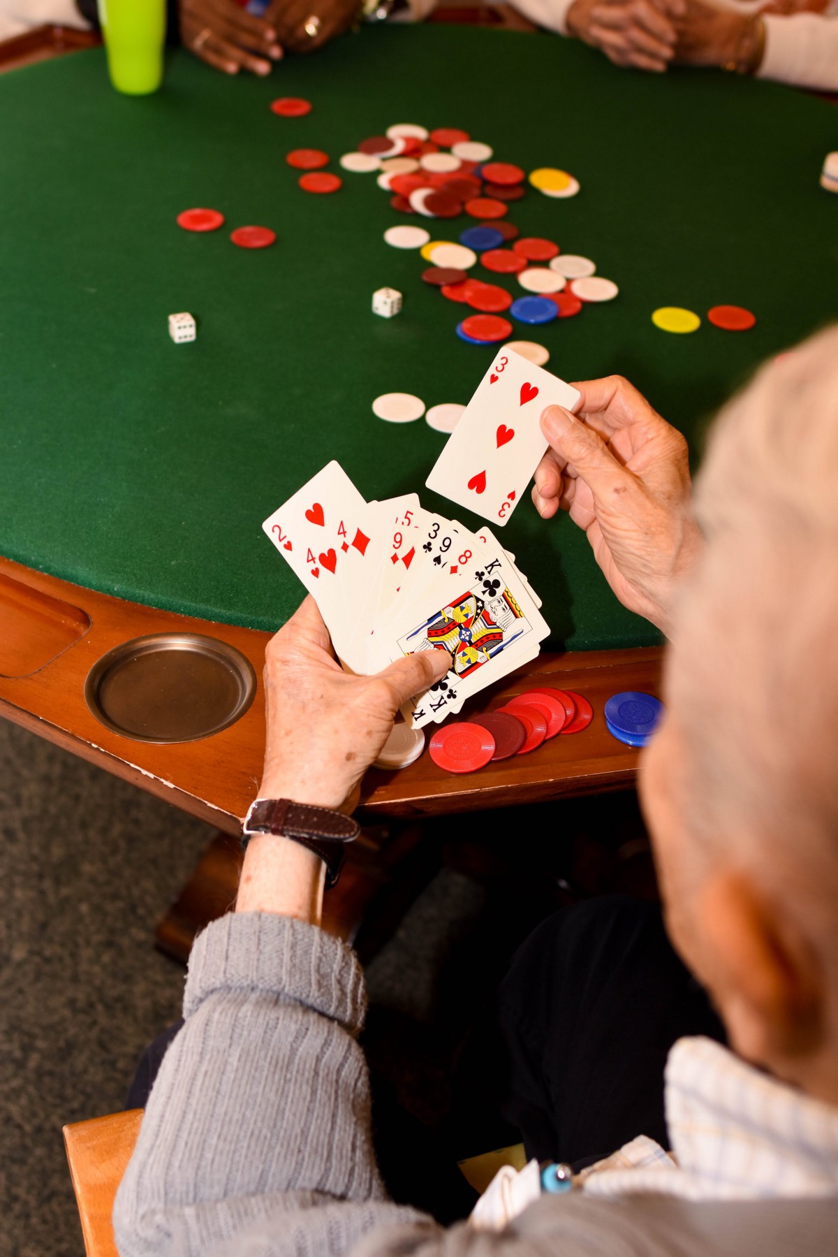 A person holding a hand of playing cards at a poker table with chips scattered.