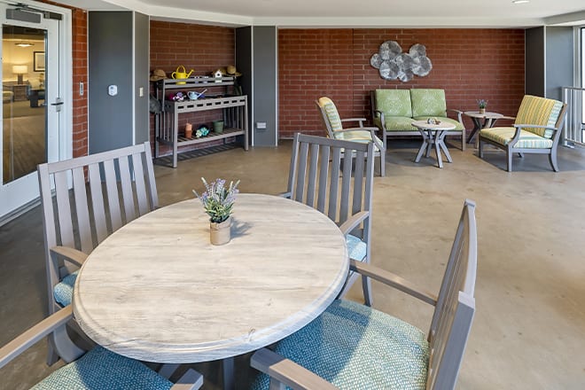 A modern lounge area featuring a wooden table with chairs and additional seating in the background.