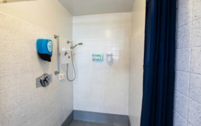 A spacious shower area with a curtain, featuring a wall-mounted showerhead and soap dispensers.
