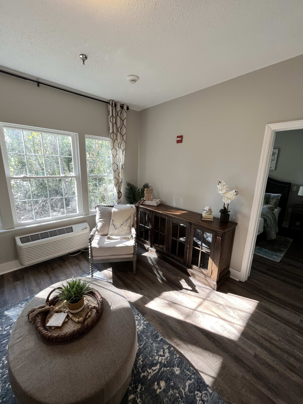 A cozy living room with natural light, featuring wooden furniture and a houseplant.