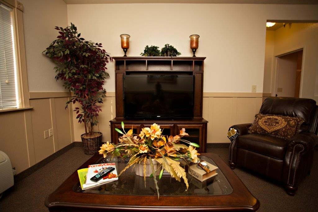 A cozy living room featuring a large television, decorative plants, and a coffee table adorned with floral arrangements.