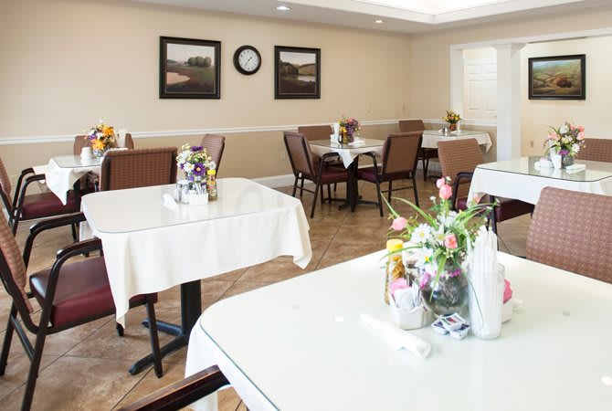 A clean and neatly arranged dining room with tables set for guests, featuring floral centerpieces.