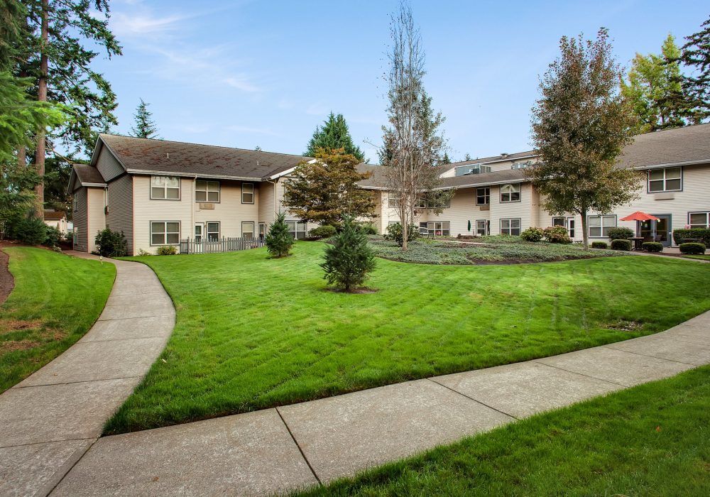 A residential apartment complex with a well-maintained lawn and trees.