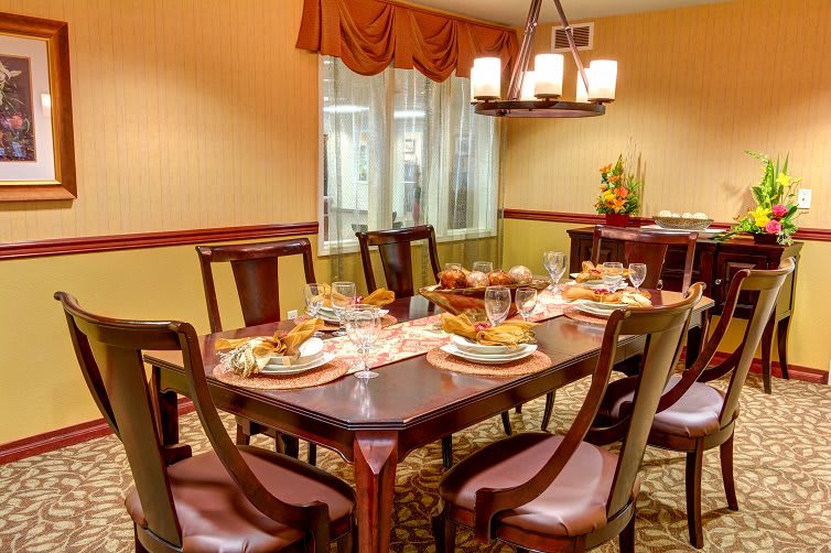 A warmly lit dining room with a table set for dinner, featuring elegant chairs and a decorative chandelier.