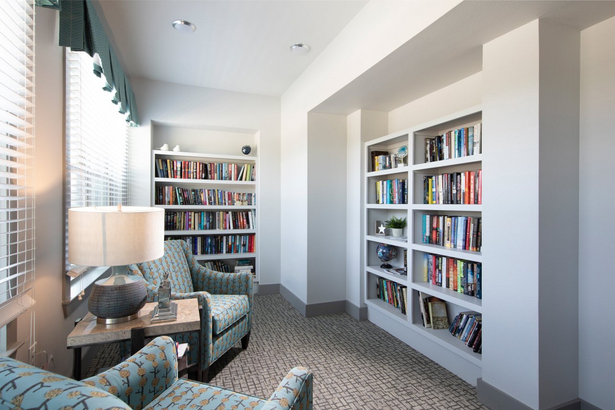 A cozy library corner with bookshelves, armchairs, and a lamp.
