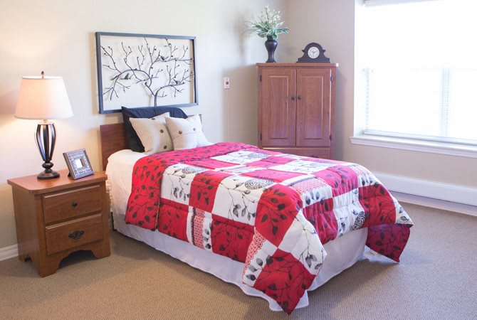 A cozy bedroom with a red and white quilt on the bed, complemented by wooden furniture and decorative elements.