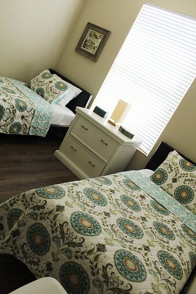 A cozy bedroom with twin beds featuring patterned bedding and a shared dresser with a lamp.