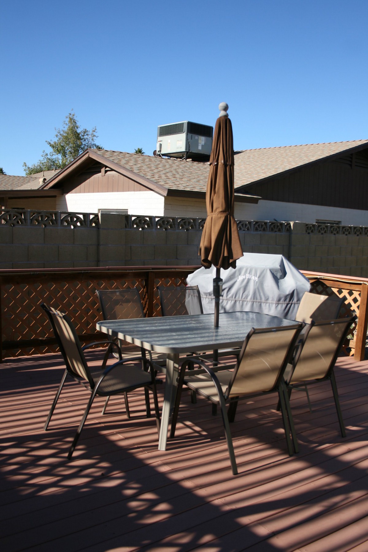 A patio with a table, chairs, umbrella, and grill on a sunny day.
