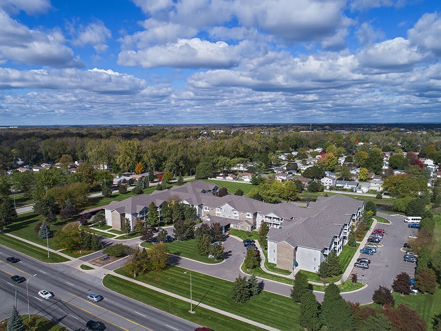 Aerial view of a residential area with an apartment complex surrounded by trees and roads under a cloudy sky.