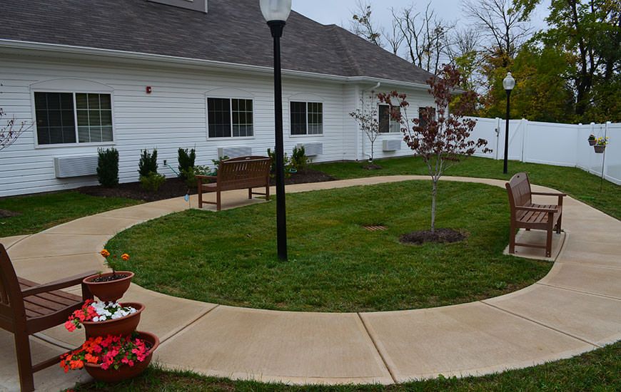 A peaceful garden area with a circular sidewalk, bench, and lamp post in front of a building.