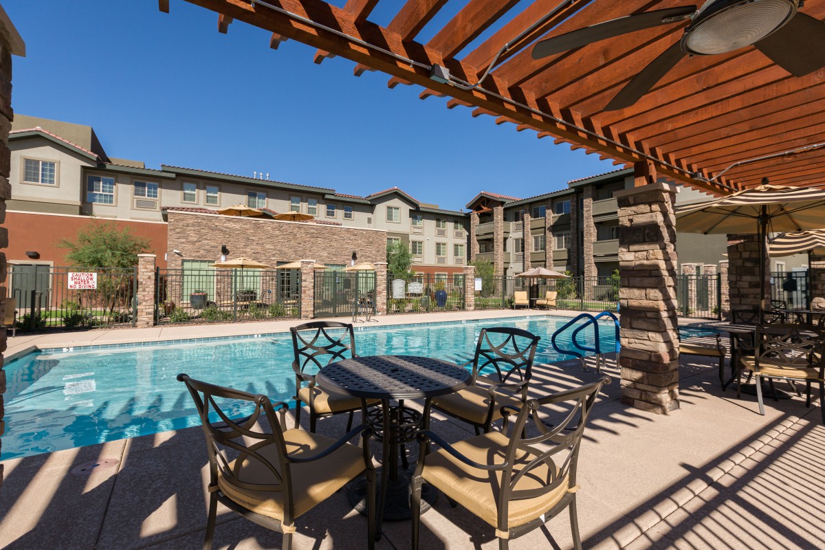A modern apartment complex featuring a swimming pool and outdoor seating area under a pergola.
