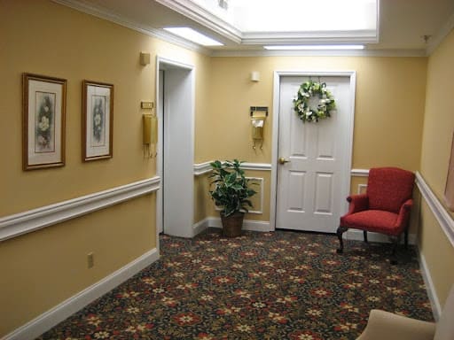 A cozy interior hallway with a carpet, red chair, plant, and decorated door.