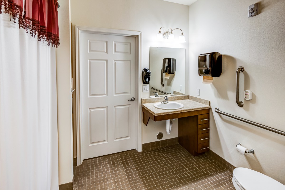 An accessible bathroom with a sink, mirror, hand dryer, and grab bars.