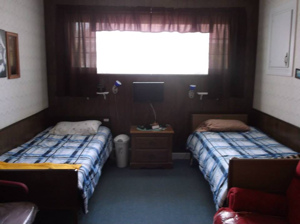 A small bedroom with two twin beds separated by a nightstand and a large window with curtains.