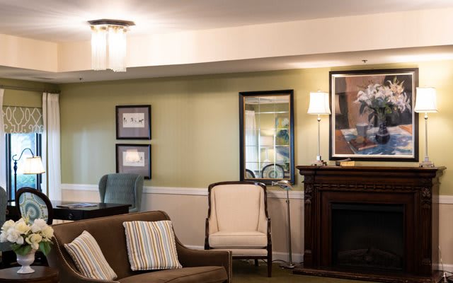 A cozy living room with a sofa, armchair, and fireplace complemented by wall art and a mirror.