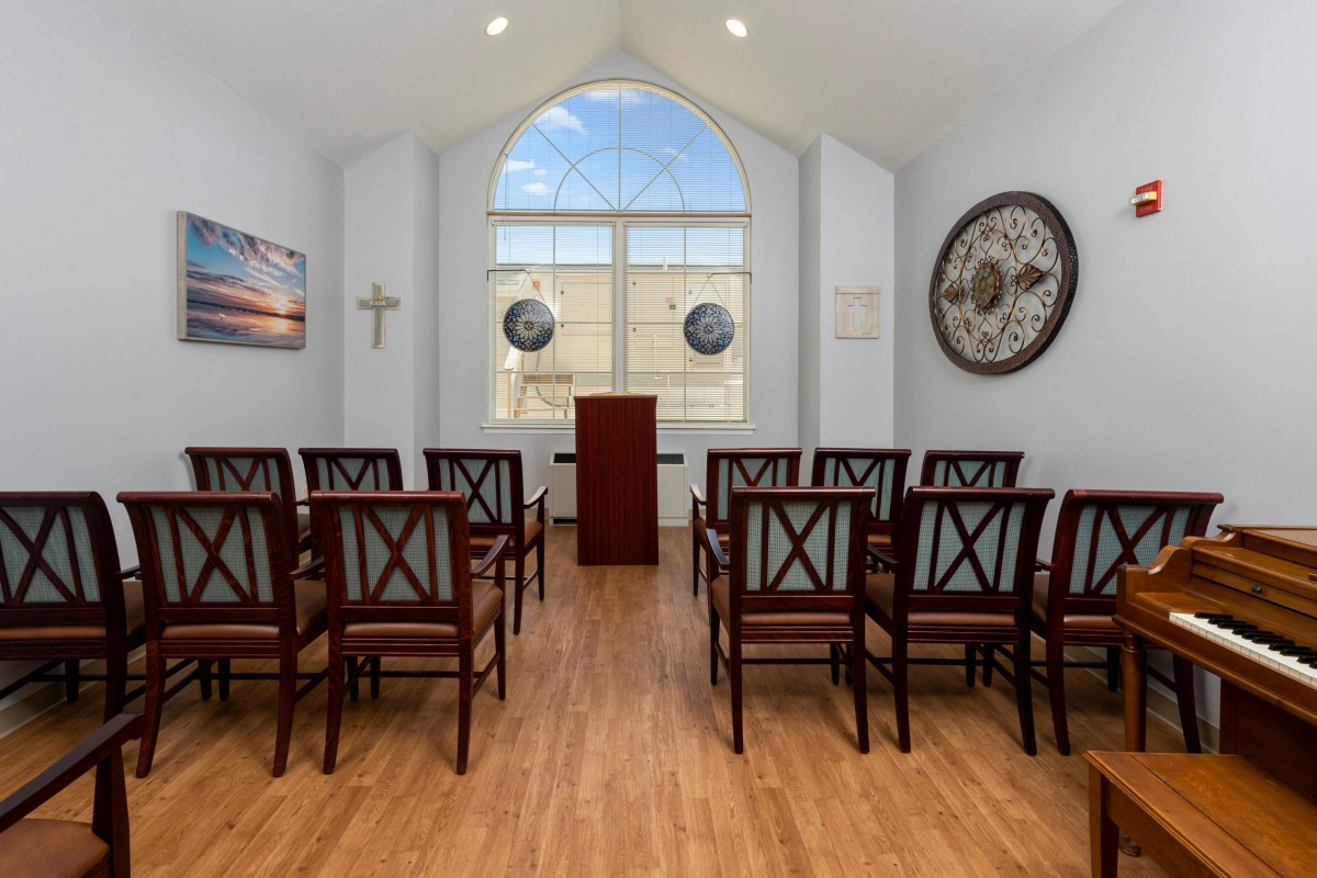 A small chapel with rows of wooden chairs facing a pulpit, decorated with a cross and artwork.