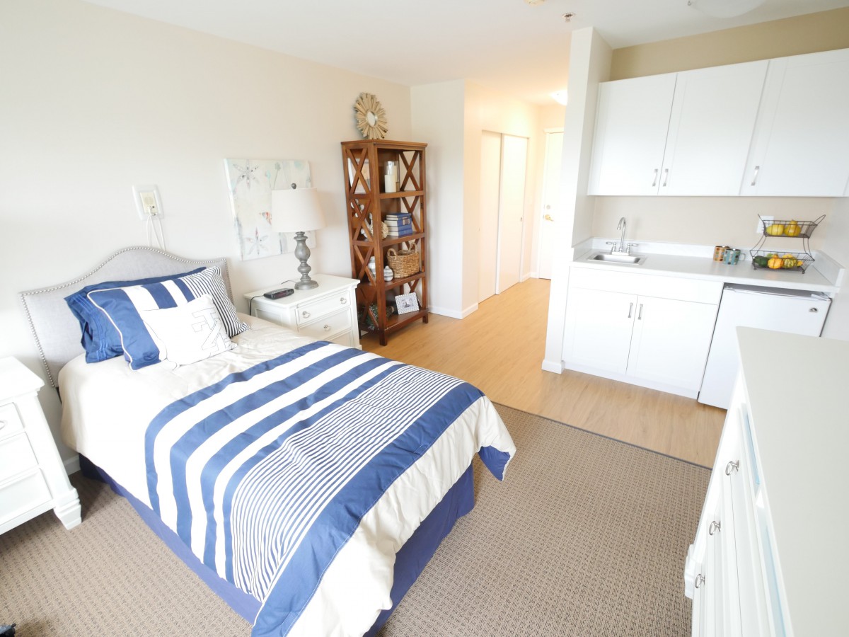 A cozy bedroom with a single bed featuring striped bedding, a shelf, and minimalist decor.