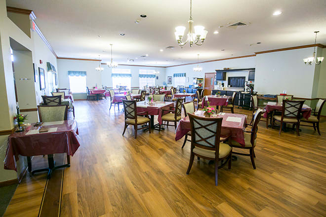 A spacious dining area with multiple tables and chairs, featuring a chandelier and wooden flooring.