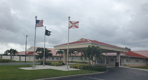 Entrance of a building featuring the American and Florida state flags on a cloudy day.