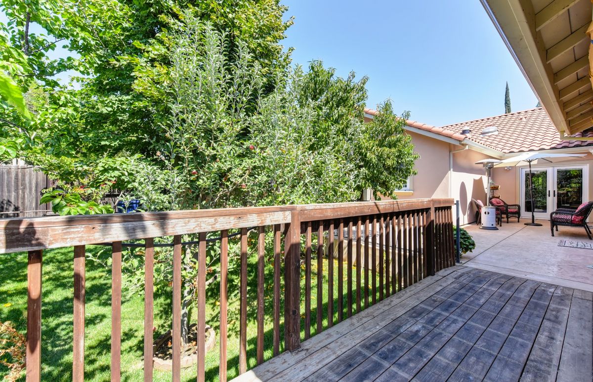A wooden deck with railing overlooking a lush backyard on a sunny day.
