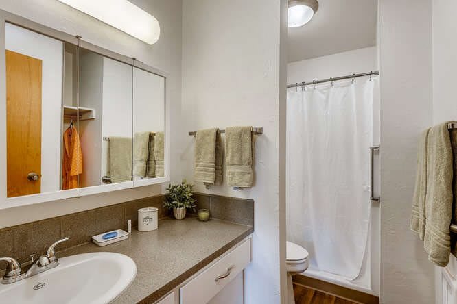 A well-organized bathroom featuring a sink, mirror, towels, and a shower area with a white curtain.