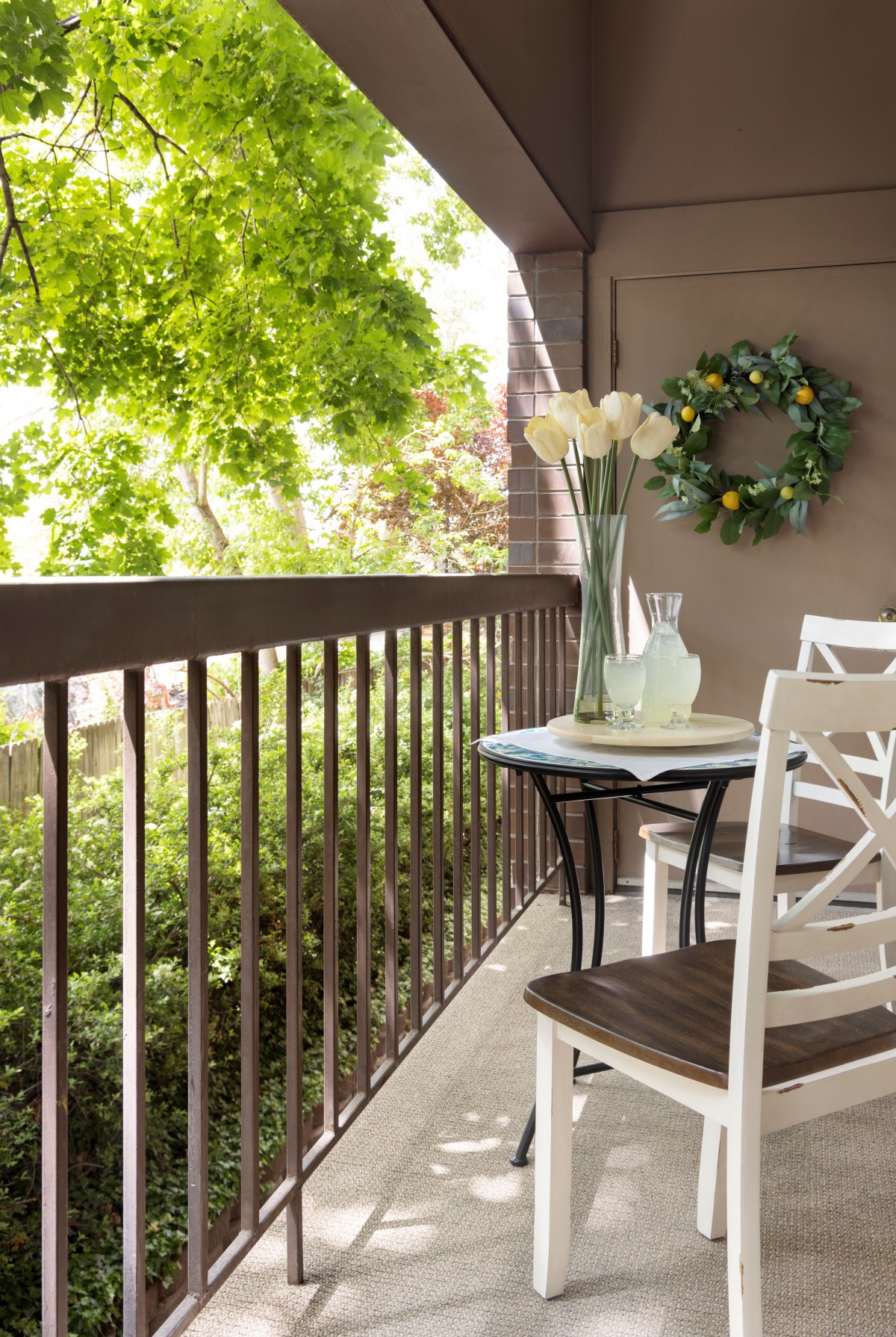 A cozy balcony with a small table and chairs, adorned with plants and a decorative wreath.