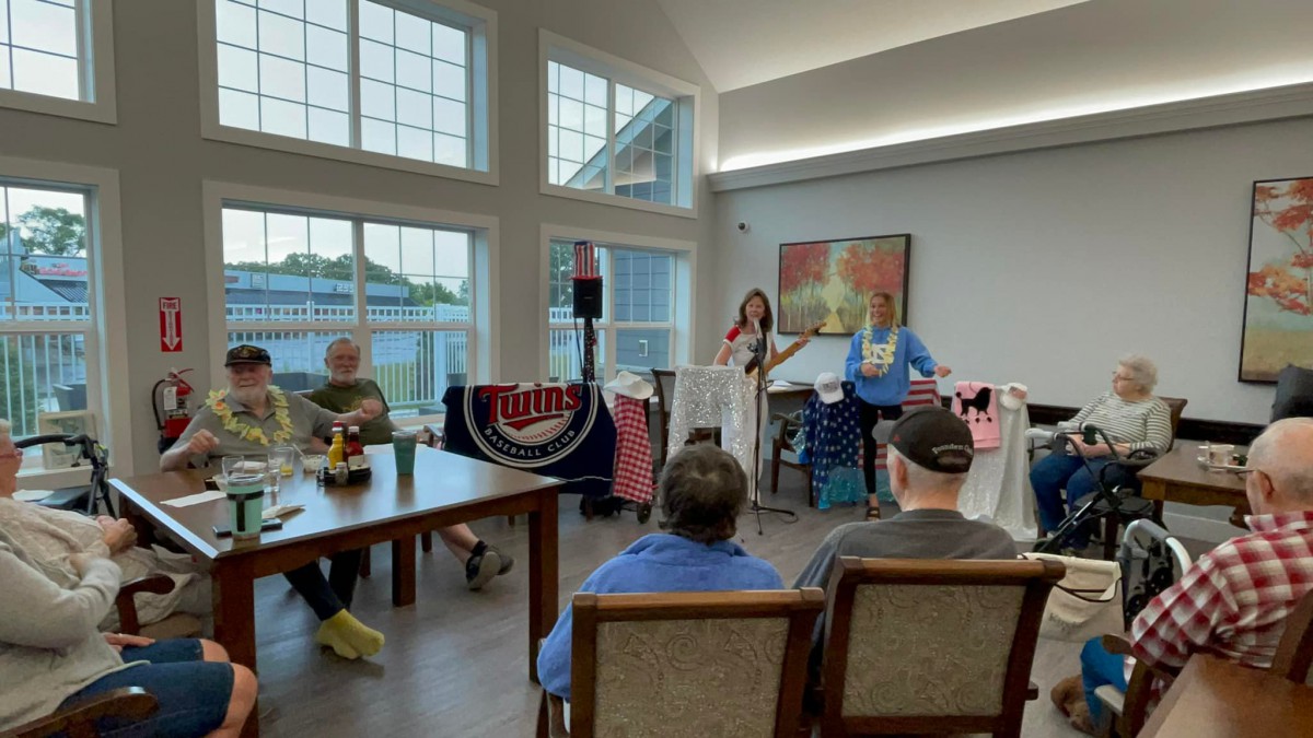 A group of people attending a presentation in a brightly lit room with large windows.