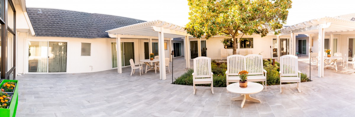 A spacious patio with outdoor furniture, including chairs and a table under a pergola, next to a house.