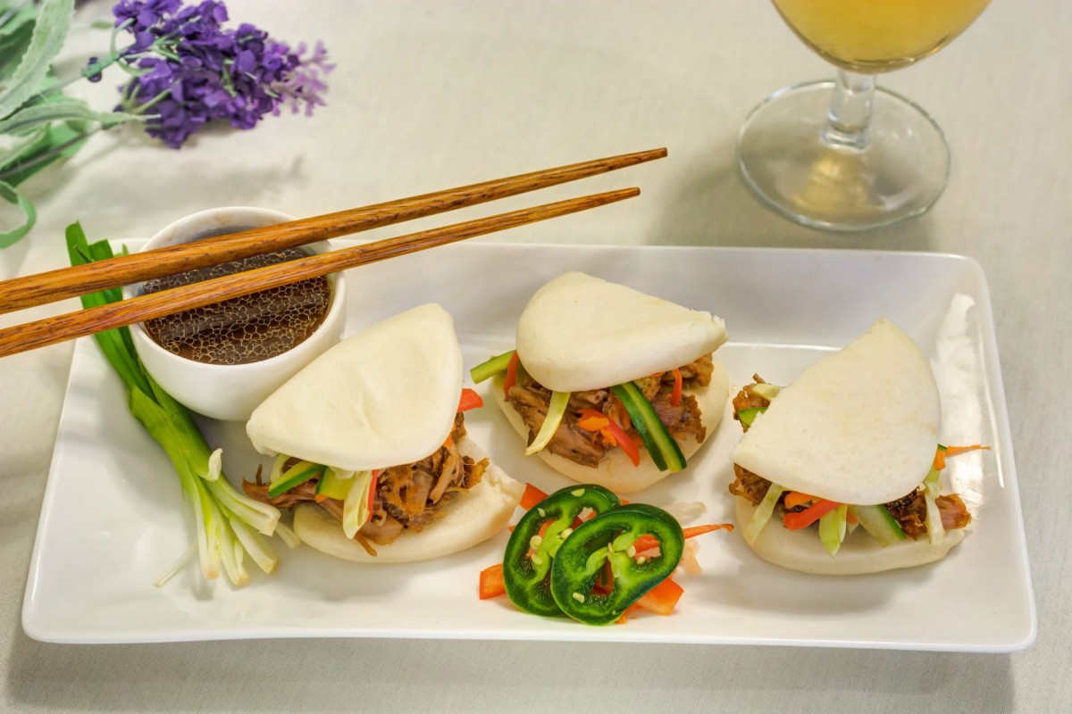 Delicious bao buns filled with savory ingredients, served with a side of dipping sauce and garnished with fresh vegetables.