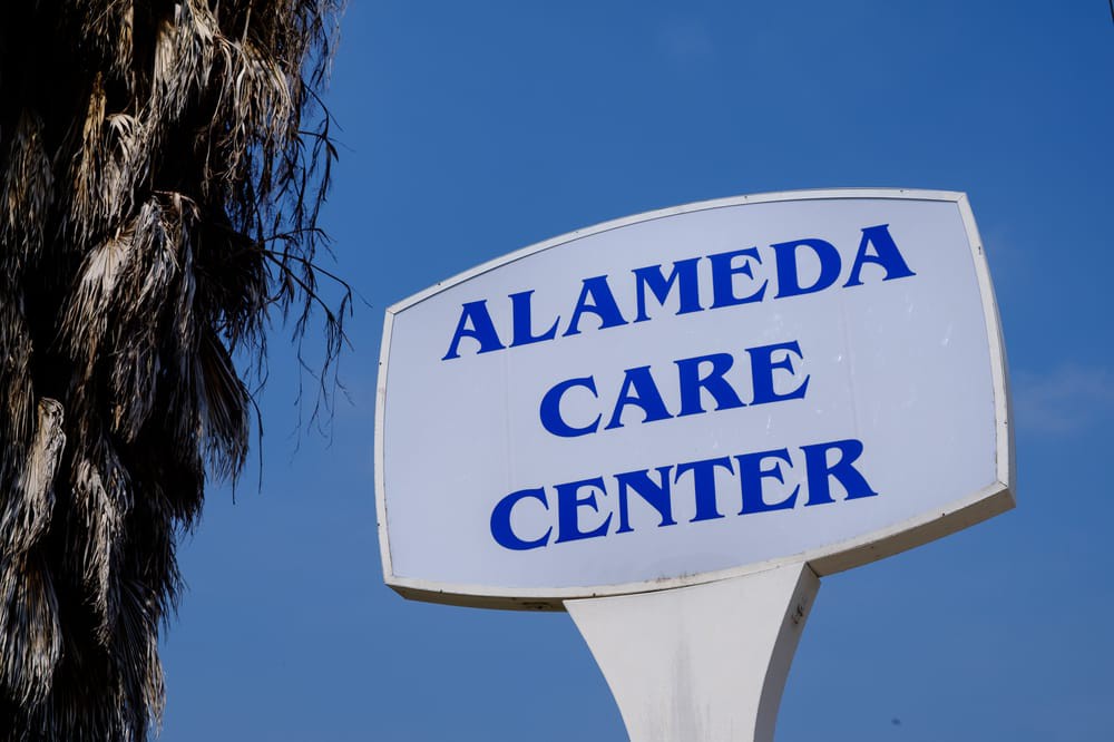 A sign for Alameda Care Center against a clear blue sky.