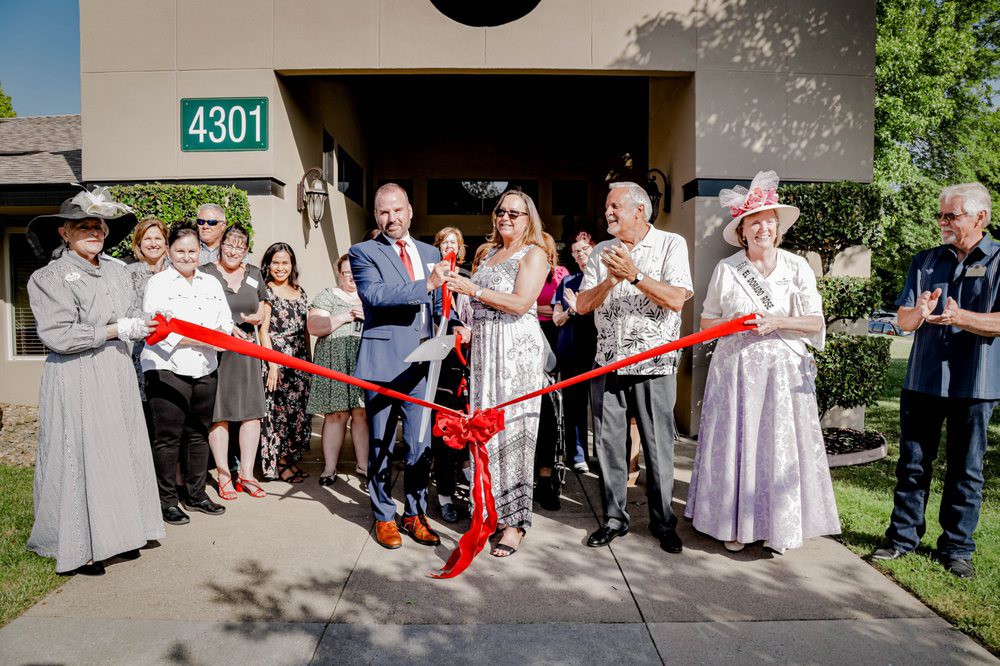 A group of people participates in a ribbon-cutting ceremony outside a building.