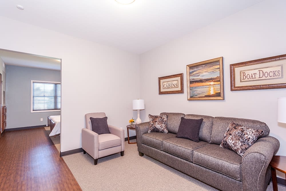 A cozy living room with a sofa, armchair, lamp, and wall artwork.