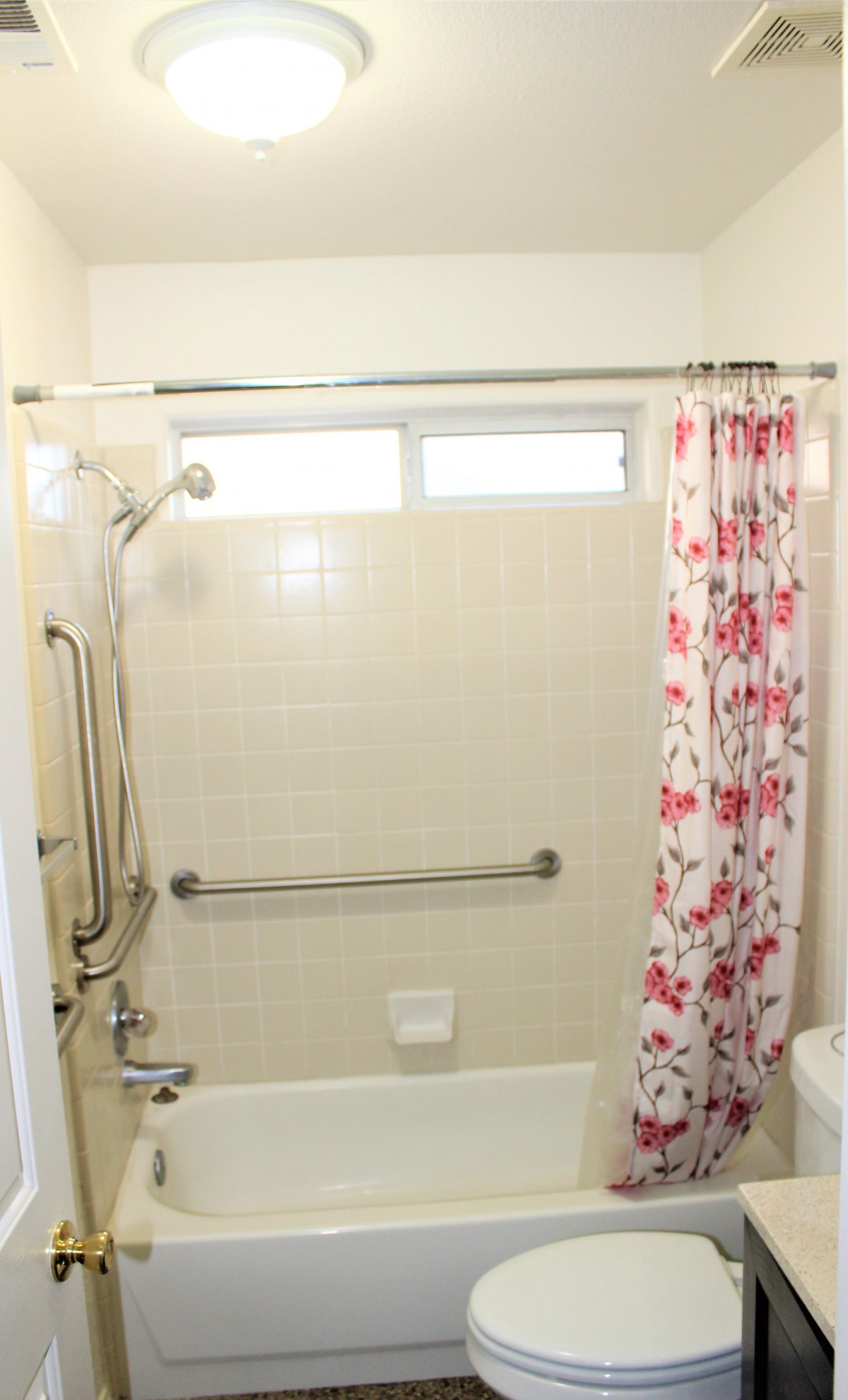 A bathroom with a shower featuring a floral curtain and safety grab bars.
